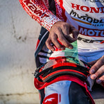 Person wearing a racing suit with visible brand logos, holding a red helmet.