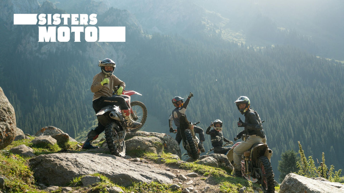 Adventure riders and their bikes on a mountain ridge above a forested valley.