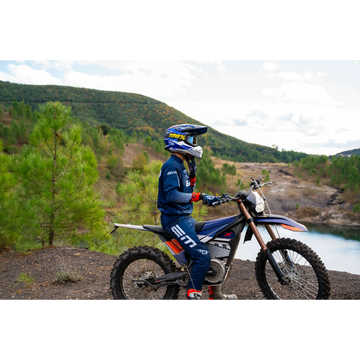 Person on a dirt bike in a scenic outdoor setting with mountains and trees.